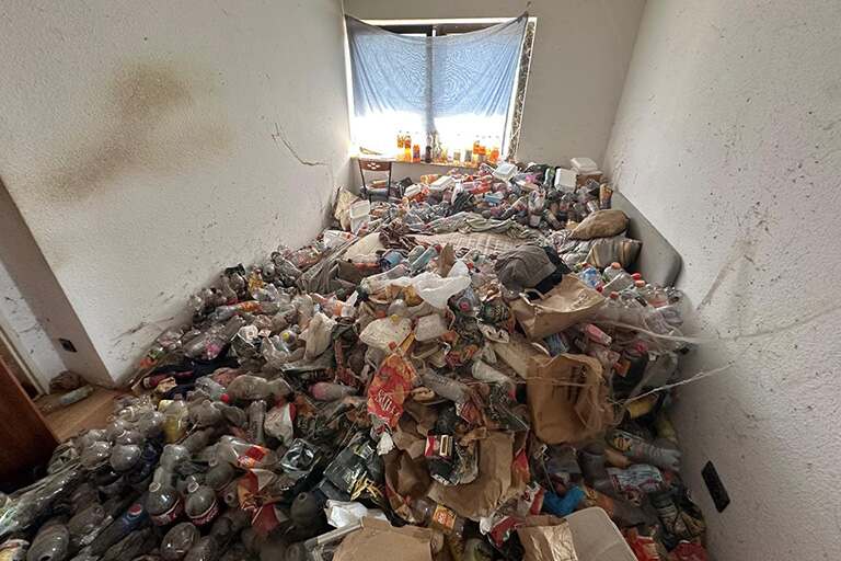 Ein kleiner, unordentlicher Raum mit Stapeln von Plastikflaschen, Tüten und diversem Müll, der den Boden bedeckt - Notfall-Hilfe: Messie Wohnung Entrümpelung.